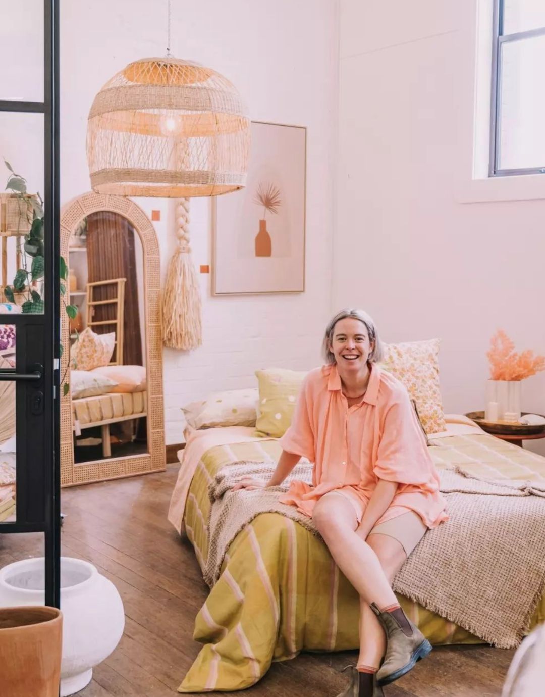 Image of Lauren Henry from Common Circus sitting on a bed in her Retail store based in Newcastle NSW. Bed styled with natural tone bed linen.